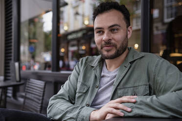 Smiling man sitting in front of glass at sidewalk cafe - AMWF00766