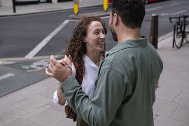 Fröhliche junge Frau mit tanzendem Mann auf dem Fußweg - AMWF00774