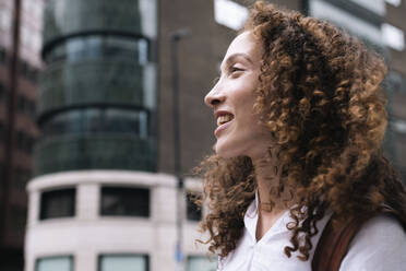 Glückliche Frau mit lockigem Haar vor einem Gebäude - AMWF00776