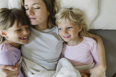 Lächelnde Geschwister entspannen sich mit ihrer Mutter im Bett zu Hause - TYF00393