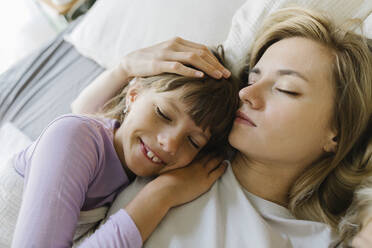 Smiling daughter sleeping with mother in bedroom - TYF00394