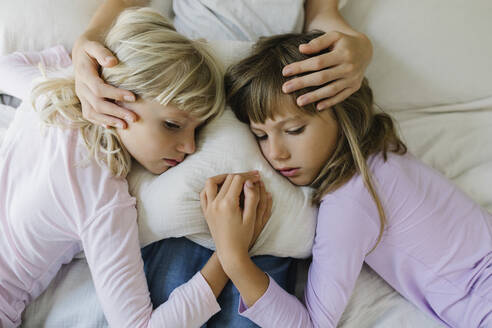 Sad siblings resting over cushion on lap of mother at home - TYF00397