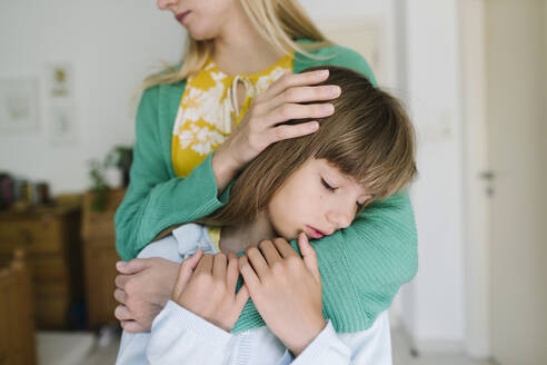 Mother hugging sad daughter from behind at home - TYF00399