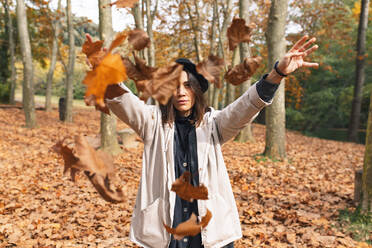 Woman throwing maple leaves standing at Fageda D'en Jorda forest, Olot, Girona, Spain - MMPF00282