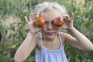 Mädchen hält sich im Garten Tomaten vor die Augen - SVKF00531