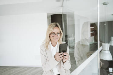 Businesswoman with glasses using mobile phone in office - EBBF06142