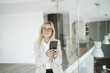 Geschäftsfrau mit Brille benutzt Mobiltelefon im Büro - EBBF06143