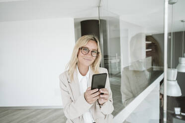 Selbstbewusste Geschäftsfrau mit Brille, die im Büro ein Mobiltelefon benutzt - EBBF06144