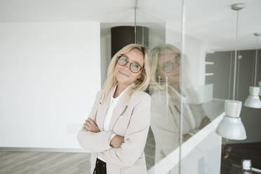 Businesswoman leaning against glass wall in office - EBBF06147