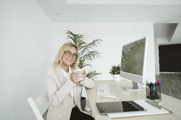 Lächelnde Geschäftsfrau sitzt am Schreibtisch im Büro - EBBF06153