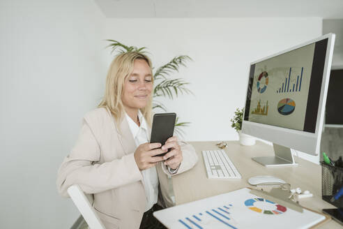 Geschäftsfrau benutzt Mobiltelefon am Schreibtisch im Büro - EBBF06168