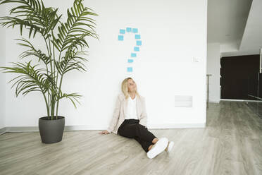 Businesswoman sitting on the floor in office with question mark above her - EBBF06176