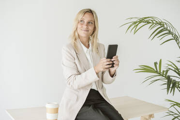 Businesswoman sitting on desk using mobile phone - EBBF06190