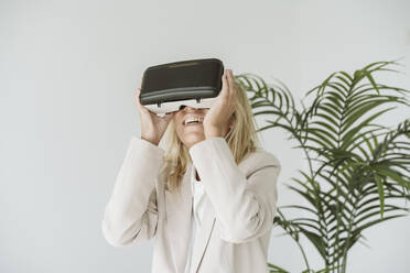 Happy businesswoman wearing VR goggles in office - EBBF06196