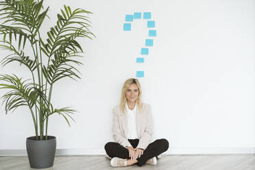 Businesswoman sitting on the floor in office with question mark above her - EBBF06211