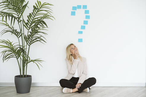 Businesswoman sitting on the floor in office with question mark above her - EBBF06212