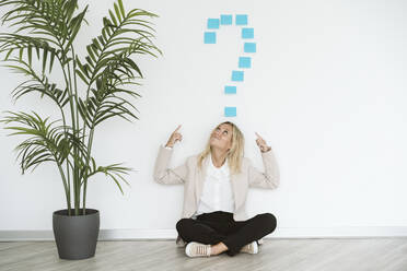 Businesswoman sitting on the floor in office pointing at question mark above her - EBBF06213