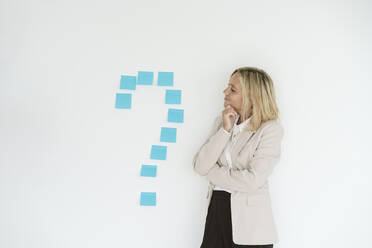 Geschäftsfrau schaut auf Fragezeichen an der Wand - EBBF06214