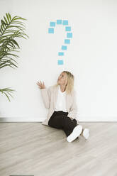 Businesswoman sitting on the floor in office looking at question mark above her - EBBF06217