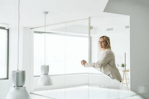 Geschäftsfrau lehnt an Geländer in minimalistischem Bürokorridor - EBBF06220