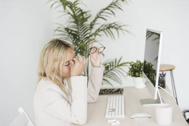 Müde Geschäftsfrau sitzt am Schreibtisch im Büro - EBBF06241