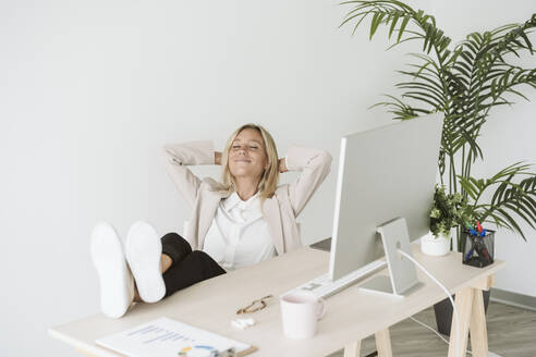 Entspannte Geschäftsfrau sitzt mit den Füßen auf dem Schreibtisch im Büro - EBBF06245