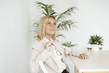 Businesswoman sitting at desk in office thinking - EBBF06257