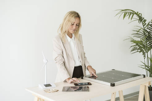 Frau, die ein Mobiltelefon mit einem Solarpanel und einem Windradmodell auf dem Schreibtisch benutzt - EBBF06261