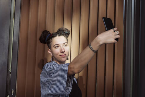 Nicht-binäre Person, die ein Selfie mit ihrem Smartphone vor einer Wand macht - OSF00832