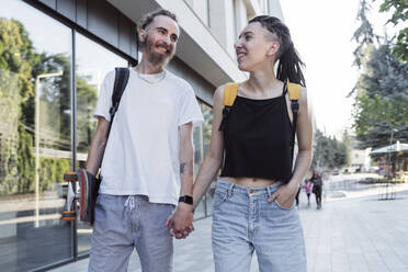 Glückliches junges Hipster-Paar, das sich an den Händen hält und auf einem Fußweg spazieren geht - OSF00845