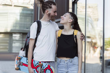 Non-binary person looking at man holding skateboard - OSF00848