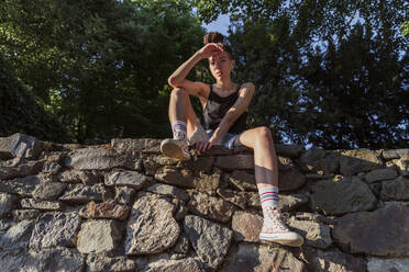 Non-binary hipster sitting on stone wall - OSF00860