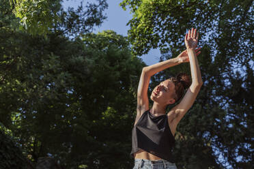 Non-binary person enjoying sunlight with arms raised - OSF00862