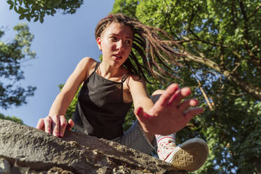 Contemplative non-binary person with locs climbing on stone wall - OSF00867