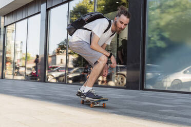 Junger Mann mit Rucksack, der auf dem Fußweg Skateboard fährt - OSF00869