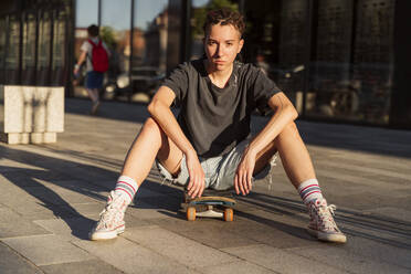 Selbstbewusste nicht-binäre Person, die auf einem Skateboard am Fußweg sitzt - OSF00872