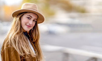 Smiling young woman with long blond hair wearing hat - GGGF01102