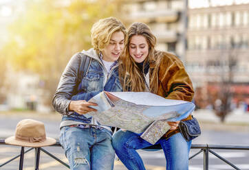 Smiling man and woman looking at map sitting on railing - GGGF01106