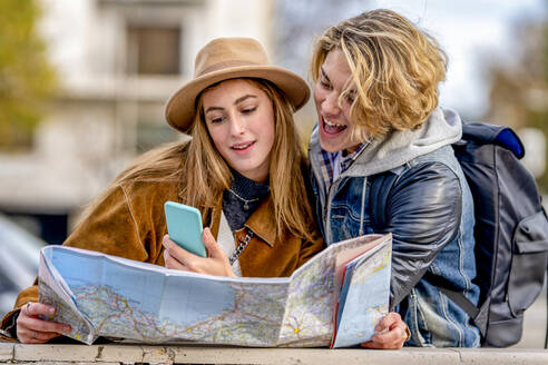 Mann teilt Smartphone mit Frau, die im Urlaub eine Karte hält - GGGF01111