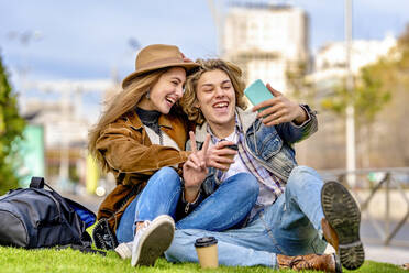 Glückliches Touristenpaar, das ein Selfie mit seinem Smartphone macht und im Park sitzt - GGGF01121