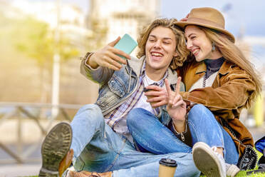 Mann zeigt Friedenszeichen und macht ein Selfie mit einem Freund durch ein Smartphone - GGGF01122