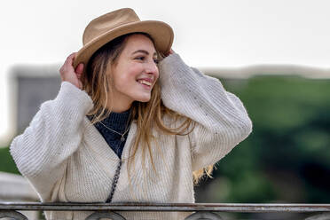 Smiling woman wearing sweater adjusting hat - GGGF01129