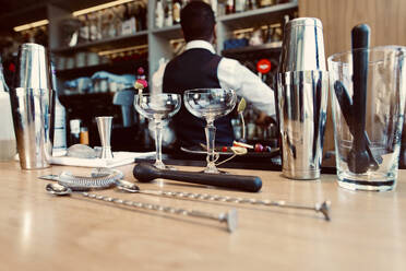 Bar equipment and glasses arranged on counter with bartender in background - GGGF01135