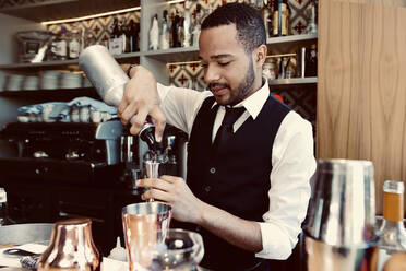 Barkeeper gießt Sirup aus einer Flasche in einen Jigger an der Bar - GGGF01136