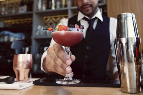 Bartender holding glass with cocktail at bar - GGGF01138