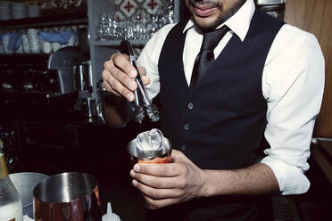 Barkeeper gibt mit einer Zange Eis in einen Shaker an der Bar - GGGF01141