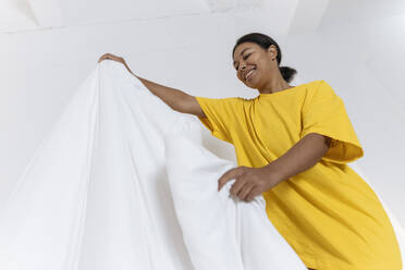 Junge Frau in gelbem T-Shirt glättet die Bettdecke im Schlafzimmer - SIF00398