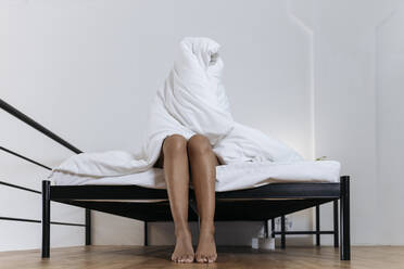 Depressive Frau sitzt auf der Bettkante und versteckt sich in einer Decke - SIF00420