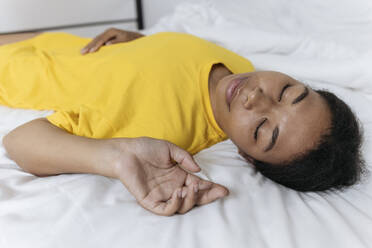 Erschöpfte Frau in gelbem T-Shirt schläft auf dem Bett zu Hause - SIF00422