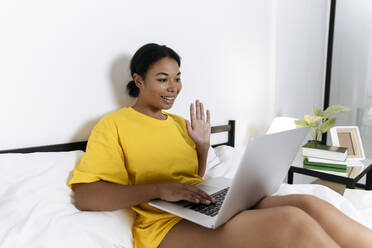 Woman having a video call on her laptop sitting in bed - SIF00443